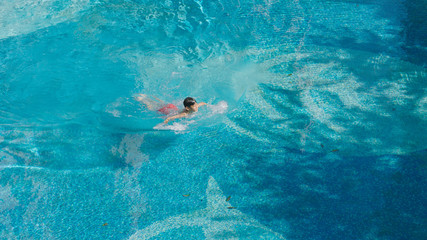 high angle view of Asian teenager swimming outdoors in blue pool