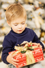 little boy in a Christmas decor with a gift in his hands