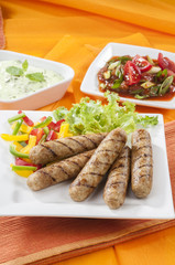 Chicken Seekh Kebabs with letus coloured bell pepper with tomato onion pickle and yogurt herb dip on white plates and on orange background