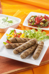 Chicken Seekh Kebabs with letus coloured bell pepper with tomato onion pickle and yogurt herb dip on white plates and on orange background