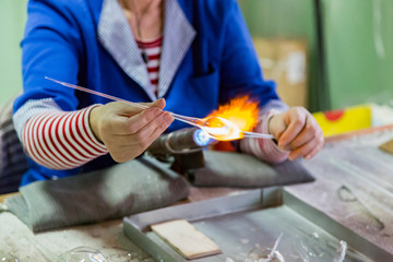 Glassblower woman works with a gas burner and a fragile glass billet
