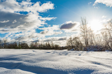 snowy field and forest during the sunset of the bright sun, blue sky with clouds, winter landscape