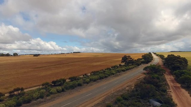 Drohnenflug im Outback von West-Australien in Richtung eines unbefangenen Highway mit einem Kornfeld im Hintergrund