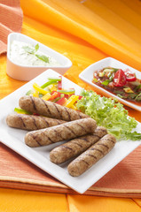 Chicken Seekh Kebabs with letus coloured bell pepper with tomato onion pickle and yogurt herb dip on white plates and on orange background