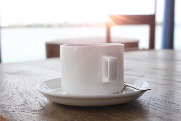 Enjoying tea at the sea beach - white ceramic  tea cup & saucer with rustic wooden table, morning sunshine & sea in the backdrop 