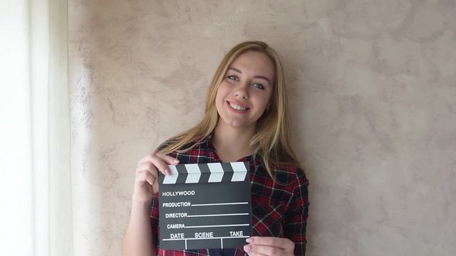 Young blonde woman actress posing with movie clapper board smiling and looking at camera