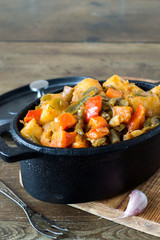 Vegetable stew. Stewed vegetables in a tall cast-iron frying pan on an old wooden table. Vegetarian cuisine. 
