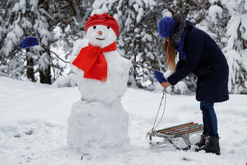 winter fun. girl in a knitted hat sculpts a snowman.