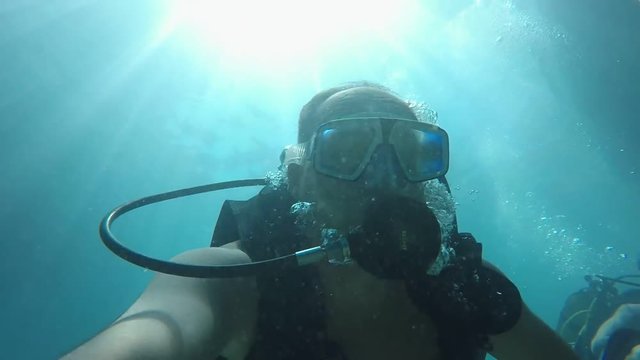 A funny view of a middle-aged scuba diver who swims underwater and makes a selfie in turquoise waters of the Mediterranean Sea in slow motion 