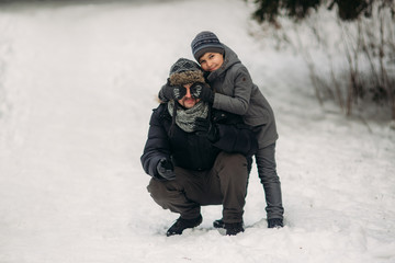 Fototapeta na wymiar Happy father with his son walks through the park in the snowy winter weather