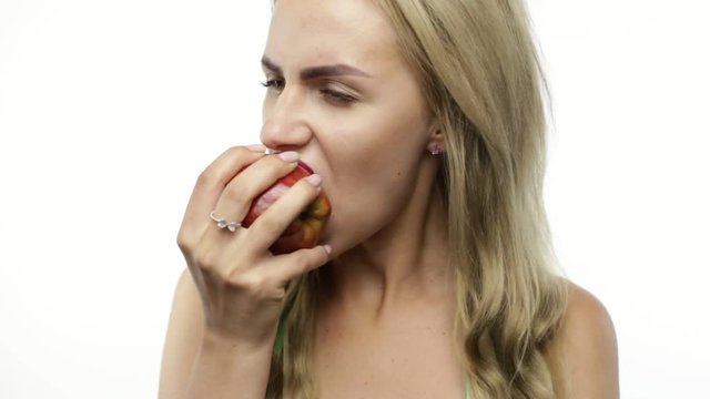 Sexy woman in bikini eating red apple on white