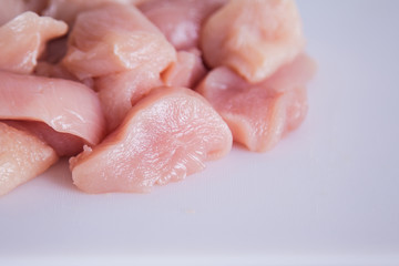 Fresh raw chicken breast cut in pieces on a white plastic cutting board