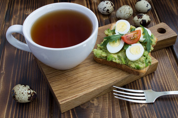 Breakfast: vegetarian sandwich with quail eggs,avocado,cherry  and tea on the wooden cutting board