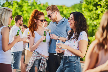 Group of people standing, drinking an having a good time at outdoor party