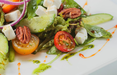 Green salad with cheese , nuts and pesto.