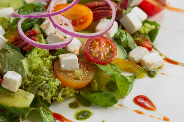 Green salad with cheese , nuts and pesto.