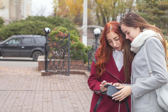 Two female teenagers looking for the news in the smartphone in the autumn city park