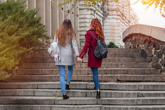 Two female teenagers walking up the stone steps holding hands in the autumn city.