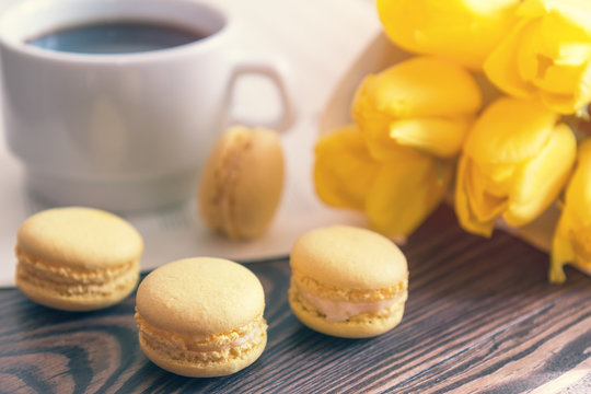 Beautiful spring music background. Cup of coffee, macaroons, yellow tulips, musical page on a dark wooden background. Shallow depth of field. Coloring photo with soft focus in instagram style