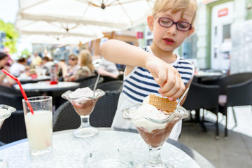 Sweet little girl with glasses is eating ice cream at restaurant, pastry shop