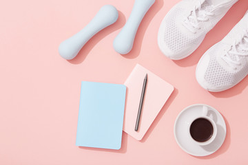 Female fitness flat lay, sneakers, dumbbells, notebook planner and coffee on pink background,...