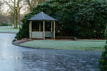 Empty and open gazebo beside pond in public park. Rhododendron shrubbery in the background....