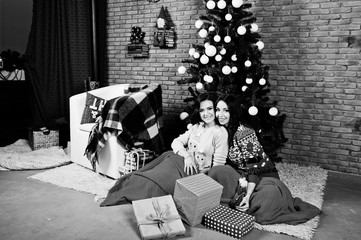 Fototapeta na wymiar Two girlfriends wear on winter sweaters sitting at room with chrismas decorations.