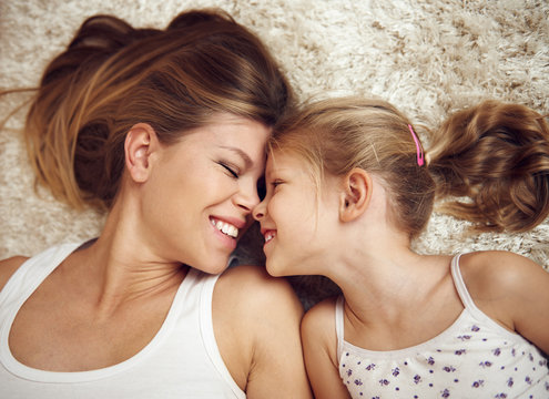 Pretty woman lying on the floor with little daughter and smiling. Concept of happiness and parenthood.