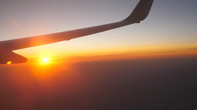 View from airplane window to beautiful sunrise or sunset. Wing of plane and cloud in sky. Travel concept. Close up