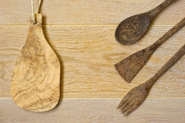 A wooden cutting board and a set of salad utensils laid out on light wooden background. 