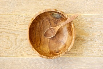 A wooden spoon in a wooden bowl on a wooden background. Top view. 