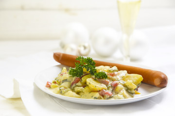 potato salad with wiener sausage and parsley garnish on a white wooden table, typical german christmas dinner, copy space