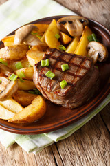Grilled fillet mignon with potato wedges and mushrooms close-up on a table. vertical