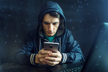 Male hacker uses the mobile phone to hack the system. Concept of cyber crime and hacking electronic...