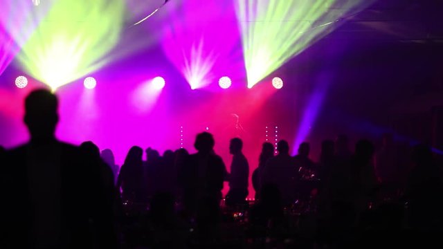 a youth party in a restaurant or a nightclub, banquet tables with alcohol and food against the background of silhouettes of dancing people, stage light and purple fill