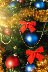 Close up Christmas tree ornaments made of glass with colored red, blue balls, golden tinsel, red bows, golden strings of beads with glitter and warm lighting detail. New Year and holiday 2018 concept.