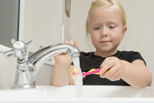 Girl Washing Toothbrush Under Running Water in Bathroom Sink