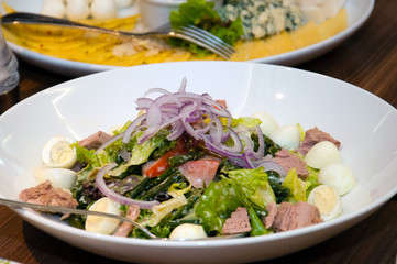 Salad from quail eggs, meat, onions, vegetables and herbs on a platter.
