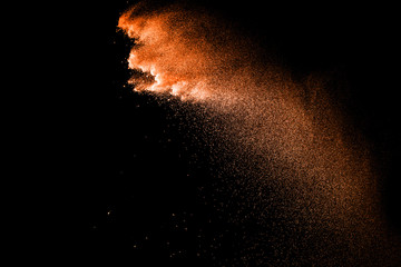 Fototapeta na wymiar Orange particles explosion on black background. Freeze motion of orange dust splash on dark background.