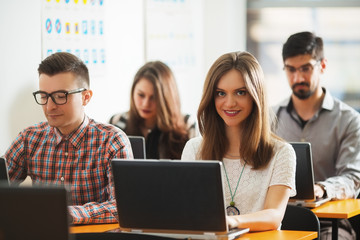 Young people in classroom siting and typing on laptop