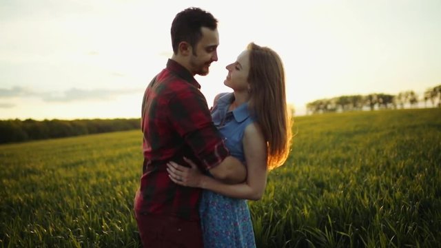 Sweet young people in love having a date in green high grass, embracing, touching their noses, kissing in cheeks on the bright sunset light.. Being happy, cheerful mood. Love story, couple goals.