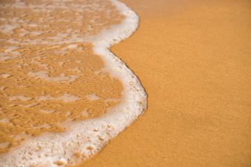 Background. A close-up of a wave runs over a sandy beach