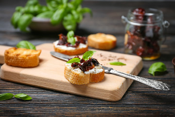 Tasty bruschetta with sun-dried tomatoes on wooden board