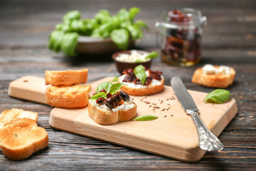 Tasty bruschetta with sun-dried tomatoes on wooden board