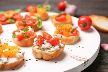 Tasty bruschettas with tomatoes on wooden board, closeup