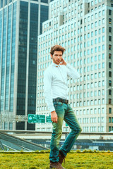 Fototapeta na wymiar Serious European businessman traveling, working in New York. Wearing white shirt, blue jeans, brown boot shoes, a young guy with beard, standing on green lawn in business district, looking at you..