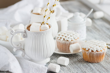 Cups with cacao and marshmallow, cupcakes and different decorations, wooden background