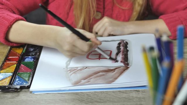 Child's hands drawing a house with paintbrush