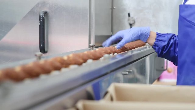 Frozen ice cream in a waffle horn is covered with chocolate glaze with nuts. Quality control of the produced ice cream. The employee looks at the ice cream on the conveyor belt.
