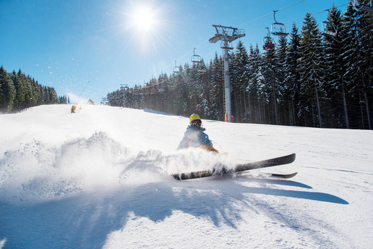 Skier falling on the slope on fresh powder snow at winter resort. Blue sky, sun and winter forest on the background copyspace adventure extreme adrenaline active lifestyle concept